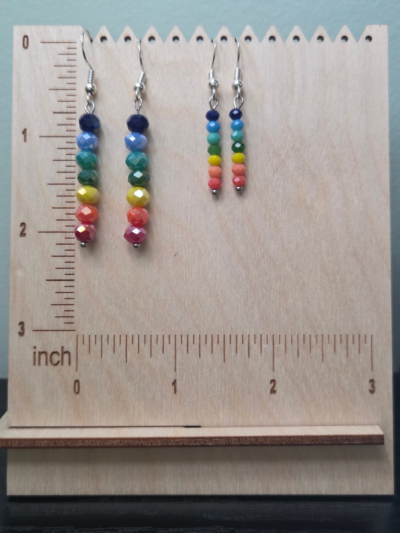 Both sizes of rainbow bead drop earrings displayed on wooden ruler board showing approximately 2 inch and 1.5 inch lengths