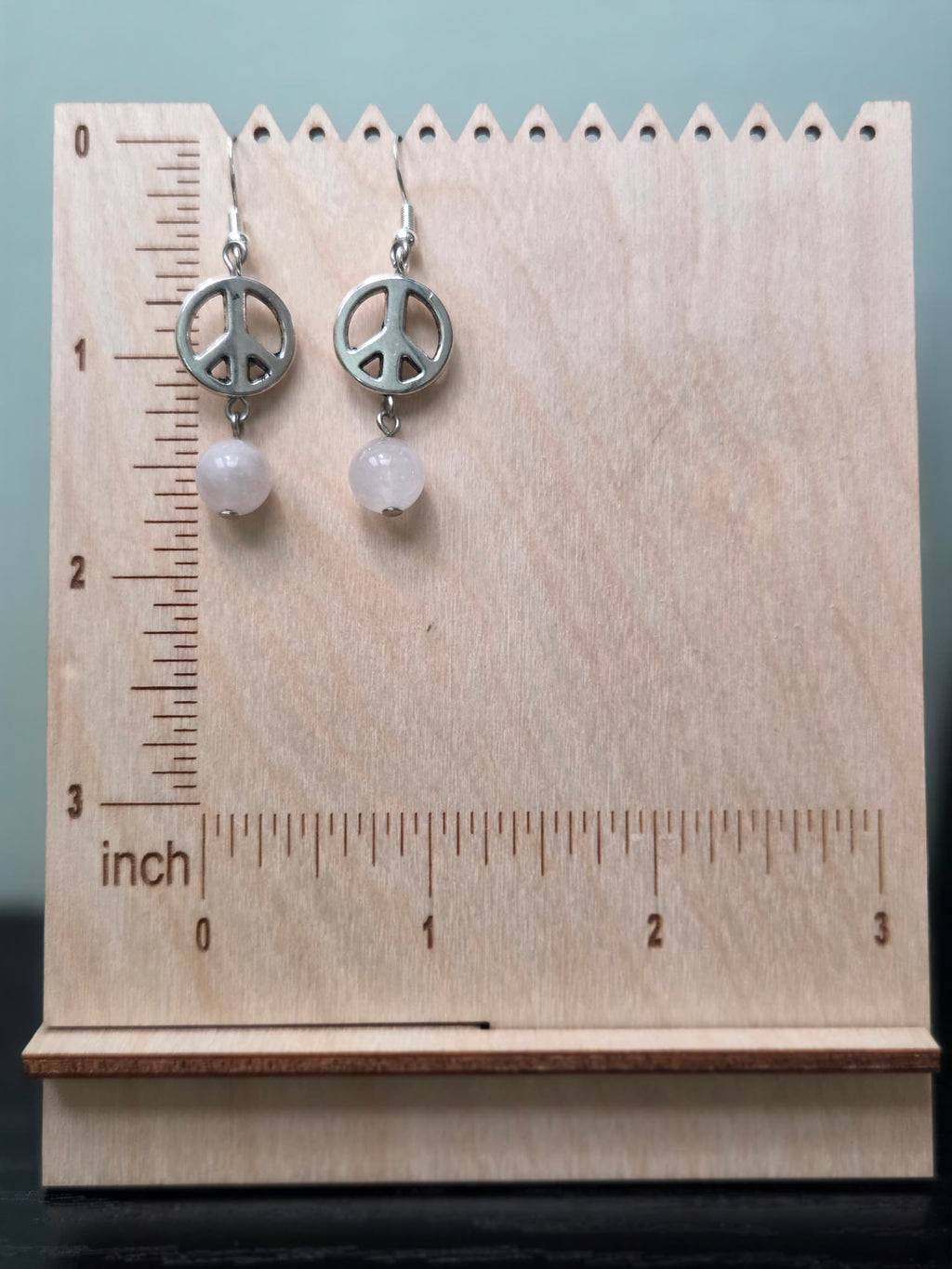 Peace sign and rose quartz drop earrings on wooden ruler board showing approximately 1.75 inch length