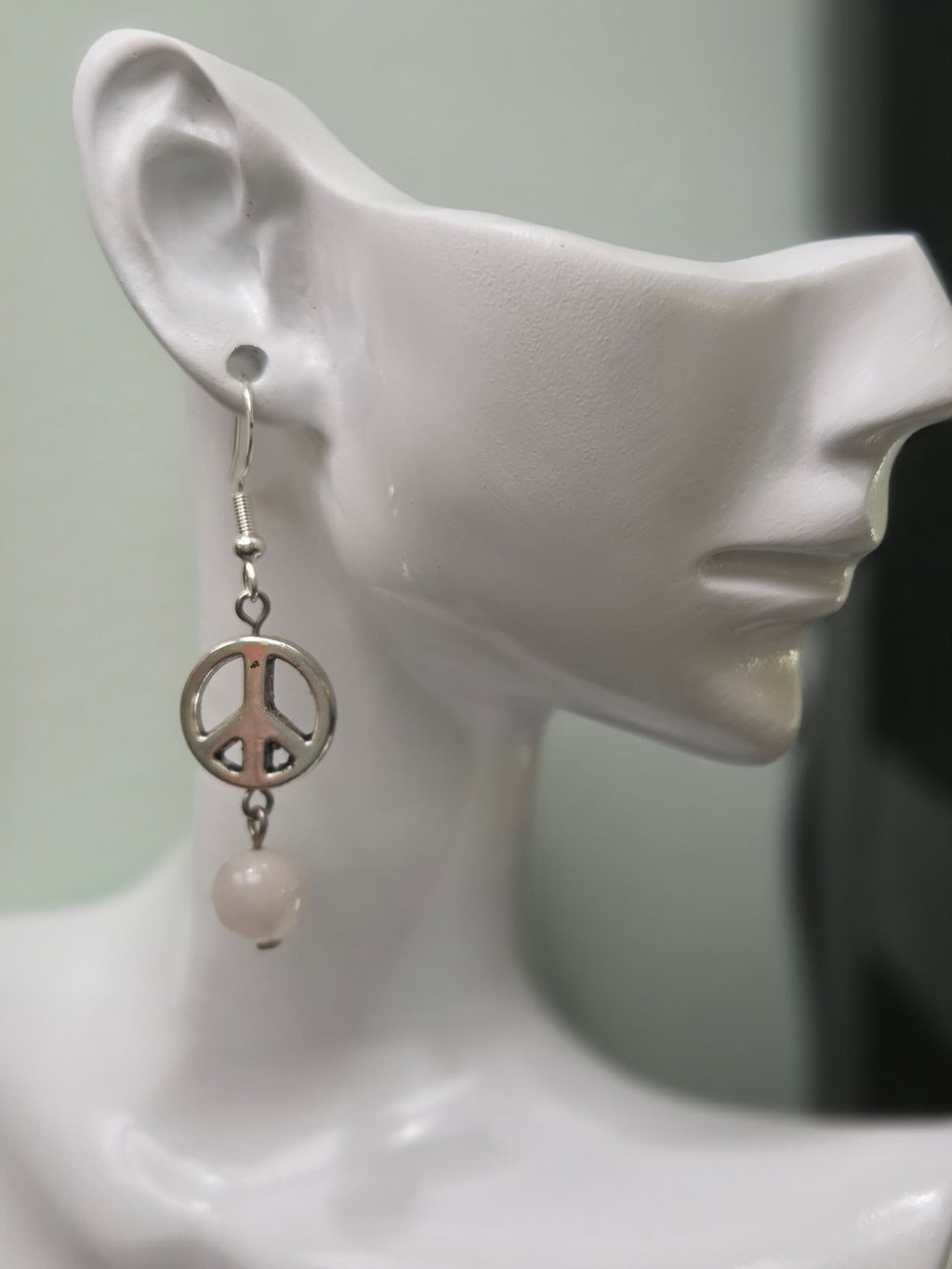 Silver peace sign and pale pink rose quartz bead drop earring worn on white mannequin ear, showing full length and movement