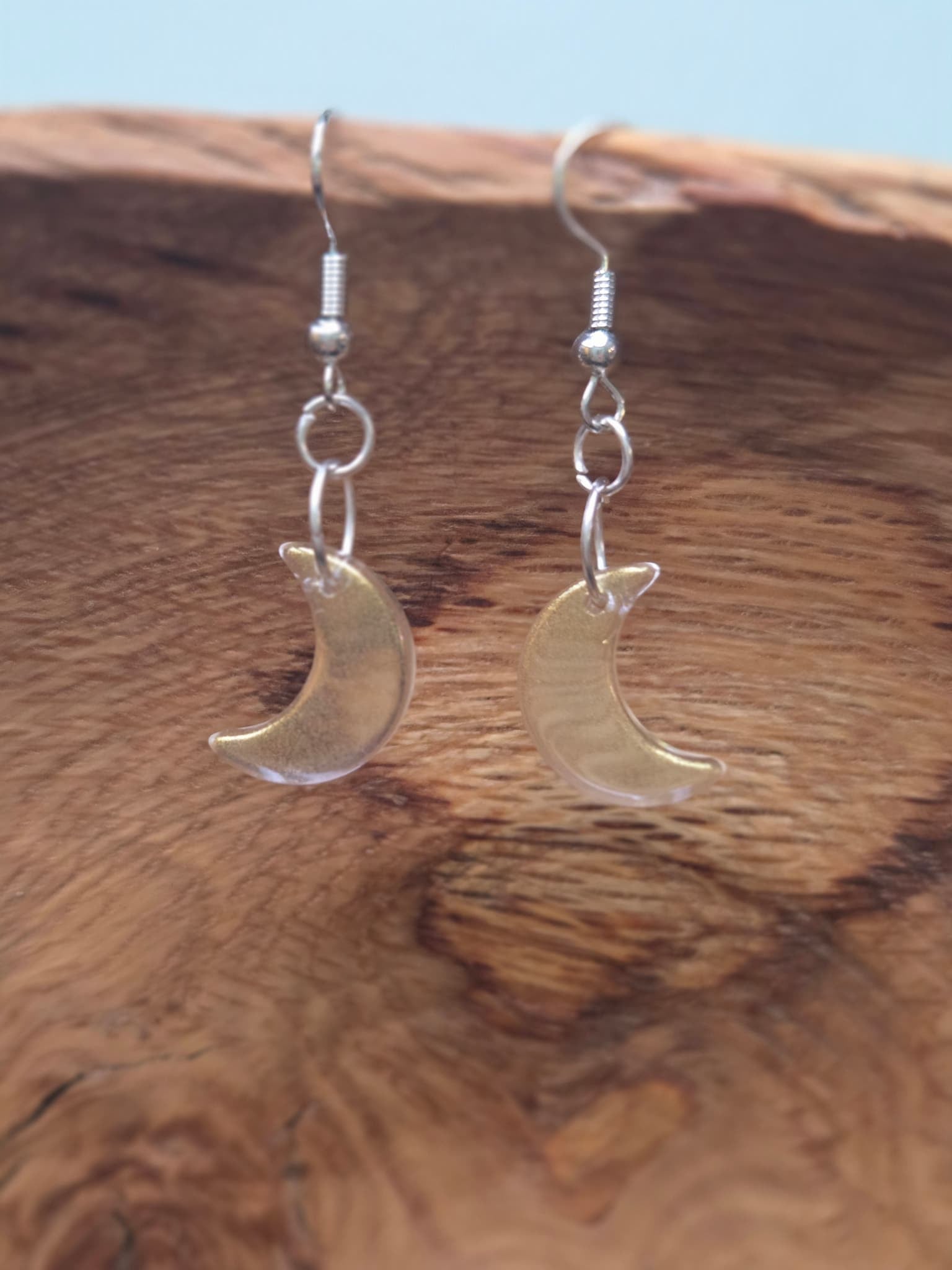 Close-up of clear iridescent glass crescent moon drop earrings displayed on rustic wood surface, showing AB shimmer finish