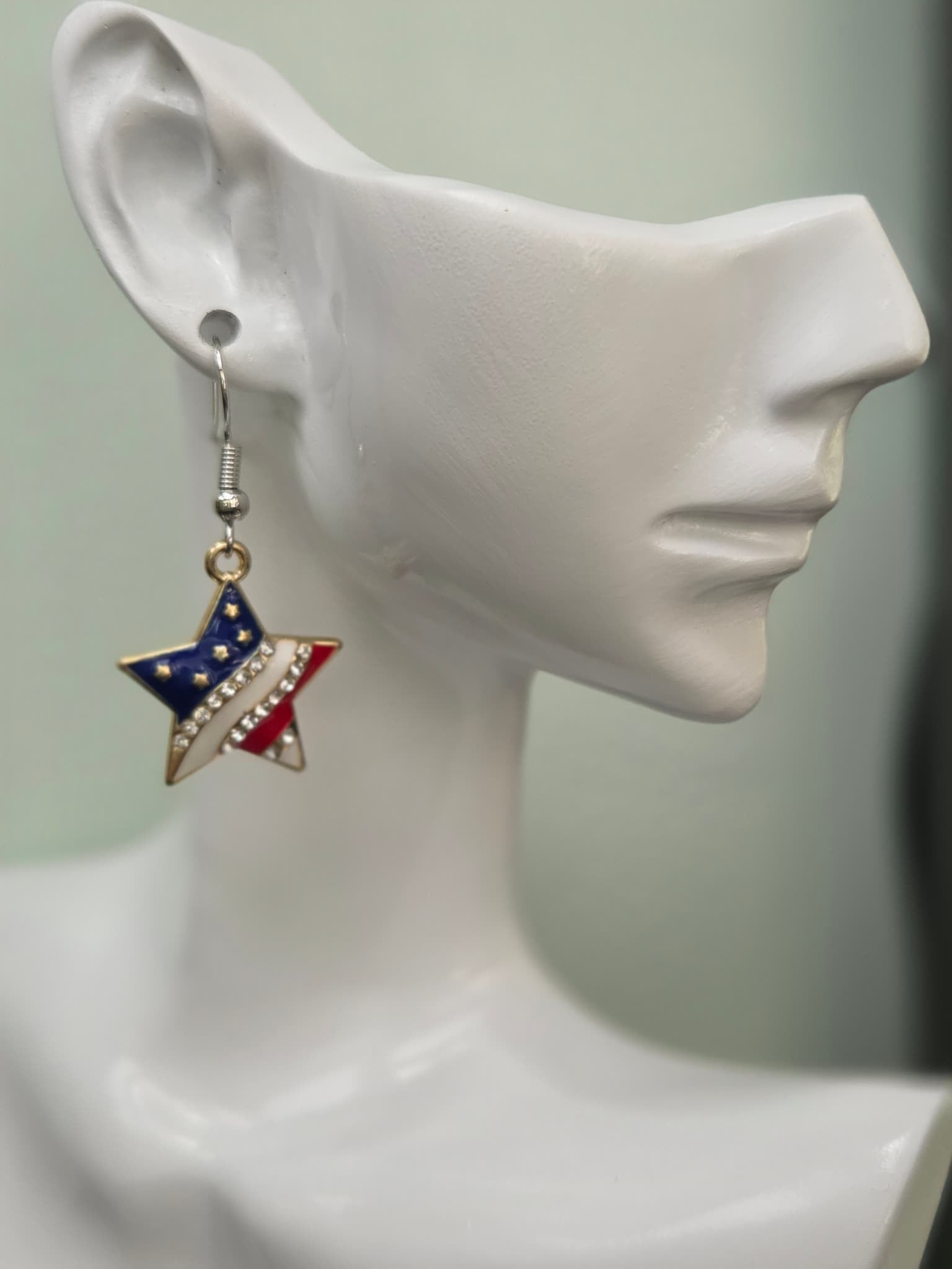 Handmade American flag star earring displayed on a white mannequin ear, featuring red, white, and blue enamel with a diagonal rhinestone band and gold-tone setting