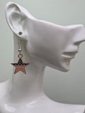 Handmade American flag bold star earring on a white mannequin ear, showcasing a star-shaped charm with wide navy blue star section and bold red and white enamel horizontal stripes in a gold-tone frame