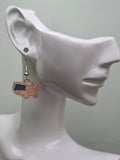 Handmade USA map-shaped earring on a white mannequin ear, featuring a continental United States silhouette filled with navy blue star corner and bold red and white enamel stripes in a gold-tone edge