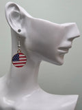 Handmade round American flag earring on a white mannequin ear, featuring a circular gold-tone bordered charm with bold red and white stripes and a navy blue corner of white stars