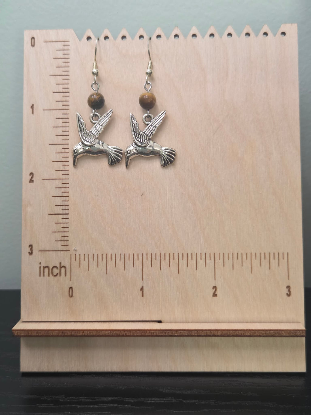 Hummingbird and tiger's eye dangle earrings displayed on a kraft card with ruler, showing full length and warm golden-brown gemstone detail