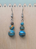Handmade graduated drop earrings featuring three round mystery stone beads swirled in sky blue, warm amber, and earthy brown, hanging from stainless steel ear wires