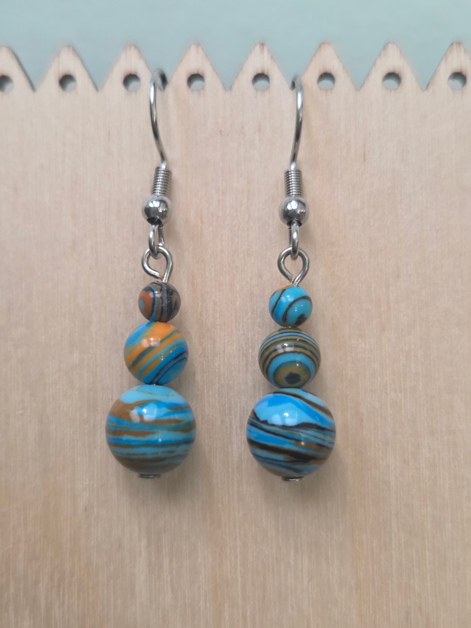 Handmade graduated drop earrings featuring three round mystery stone beads swirled in sky blue, warm amber, and earthy brown, hanging from stainless steel ear wires