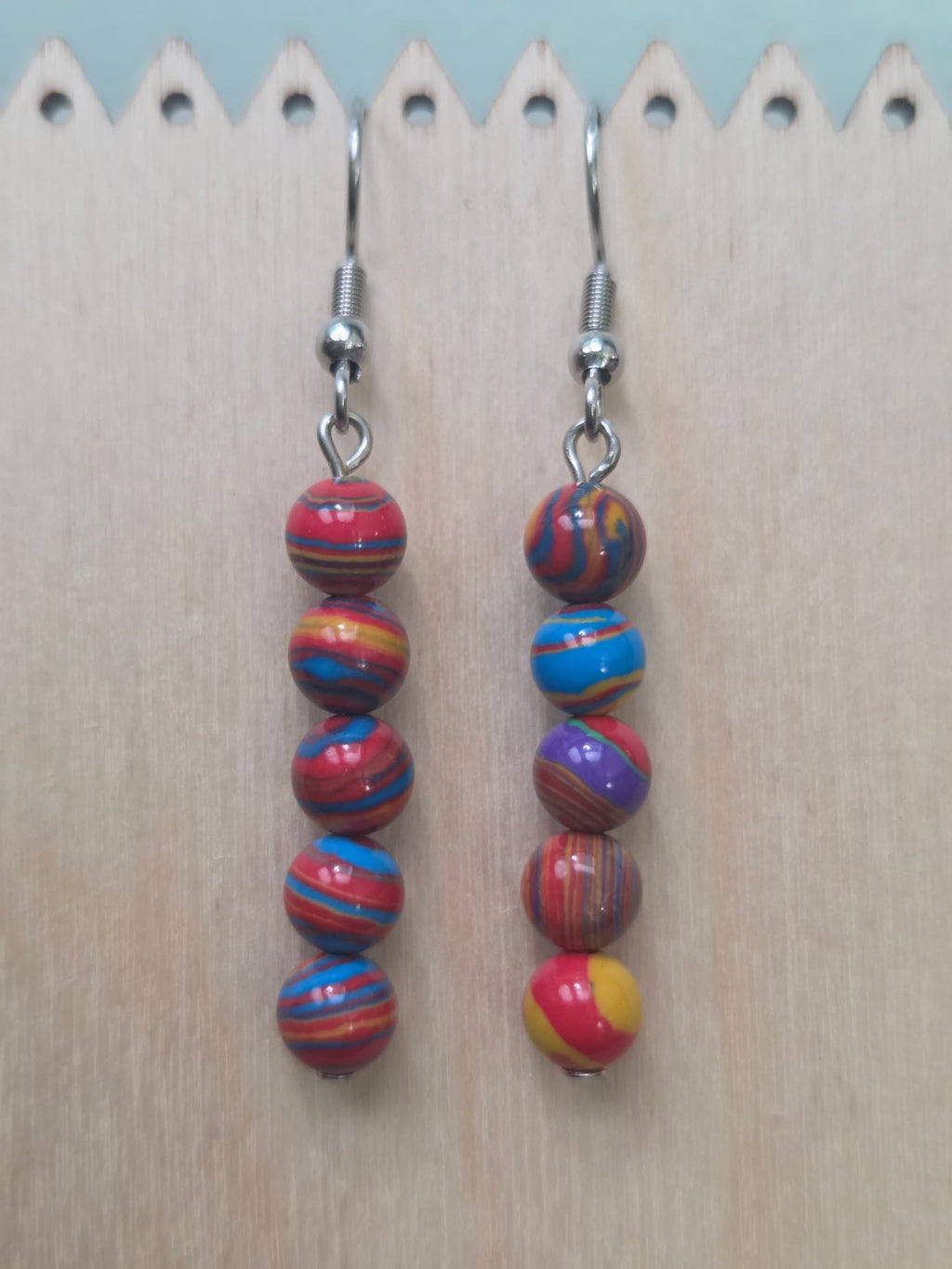  Handmade stacked drop earrings featuring five round mystery stone beads each swirled in vibrant red, blue, yellow, purple, and orange, hanging from stainless steel ear wires — two pairs shown side by side