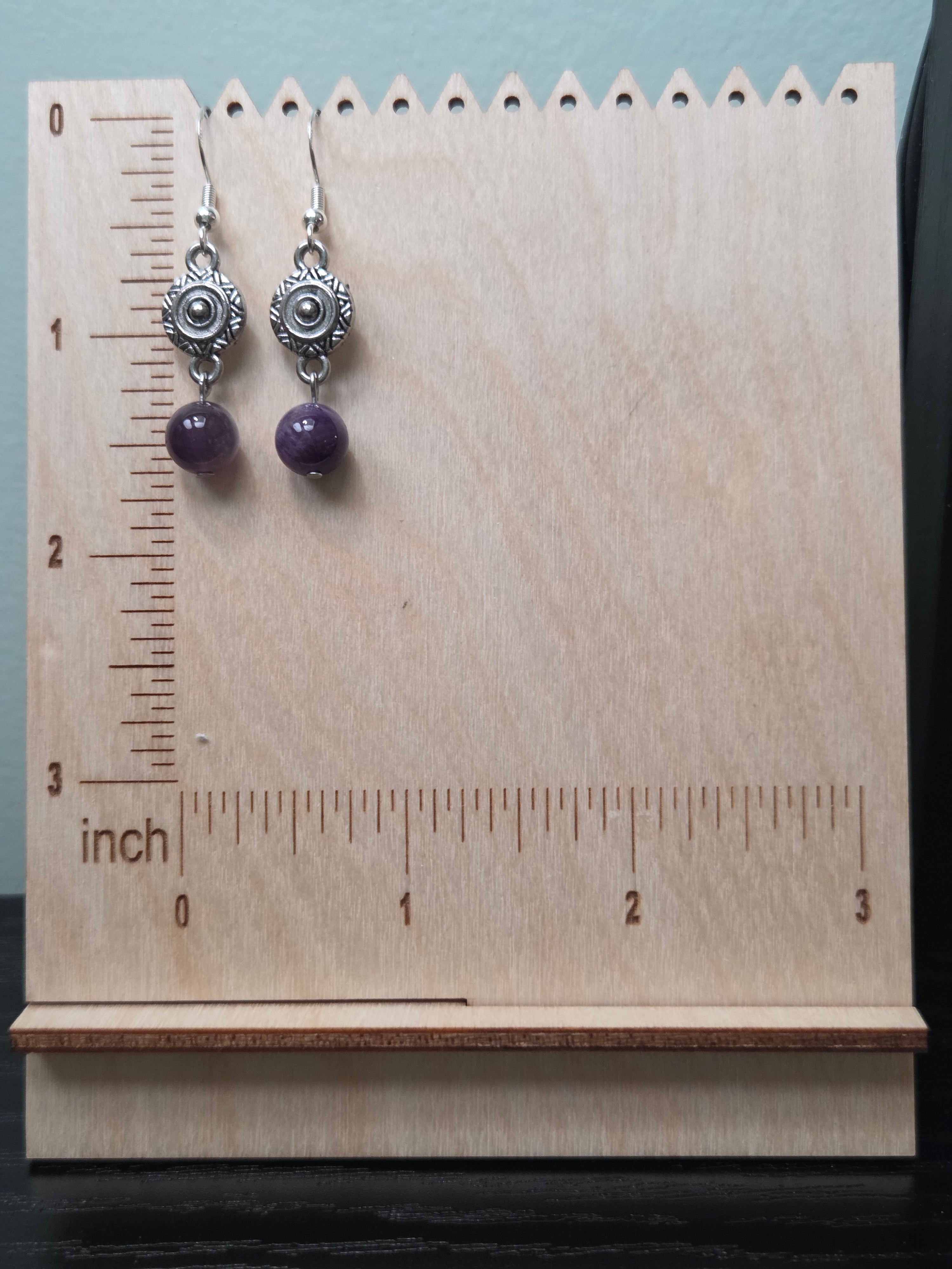Sunburst medallion amethyst drop earrings on a wooden earring stand with ruler showing approximately 1.75 inch length