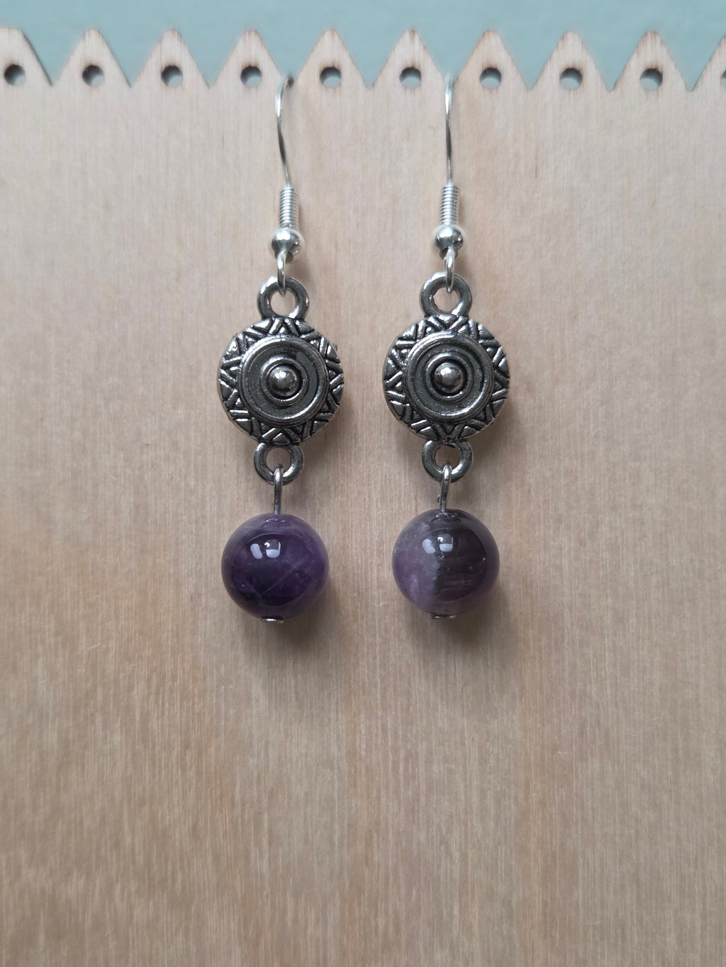 Close-up of silver-tone sunburst medallion charm earrings with amethyst round bead
