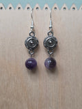 Close-up of silver-tone sunburst medallion charm earrings with amethyst round bead