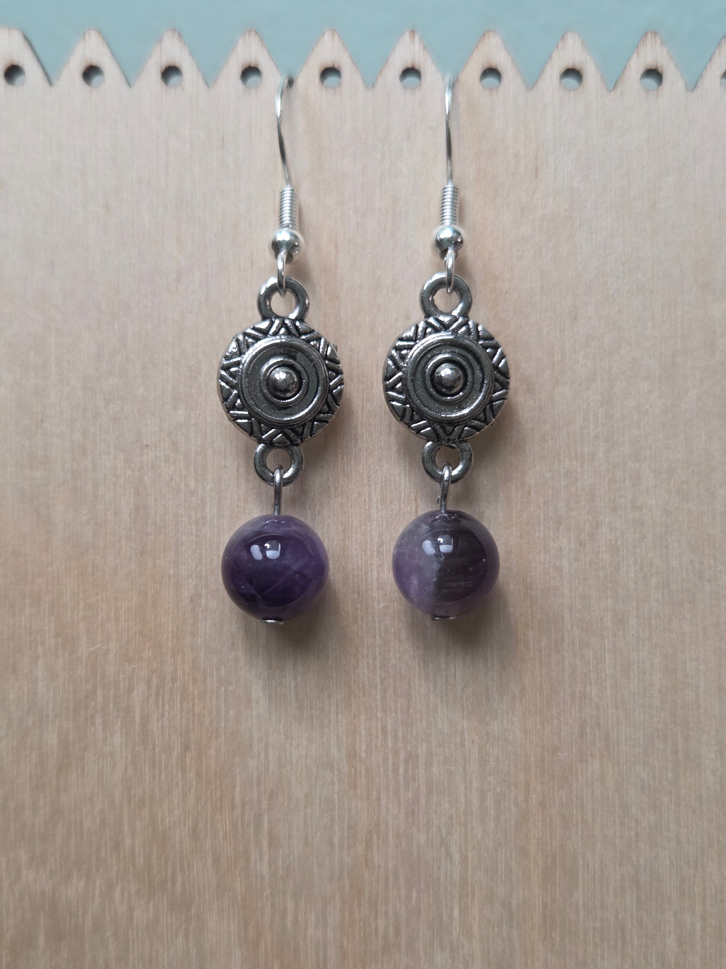 Close-up of silver-tone sunburst medallion charm earrings with amethyst round bead