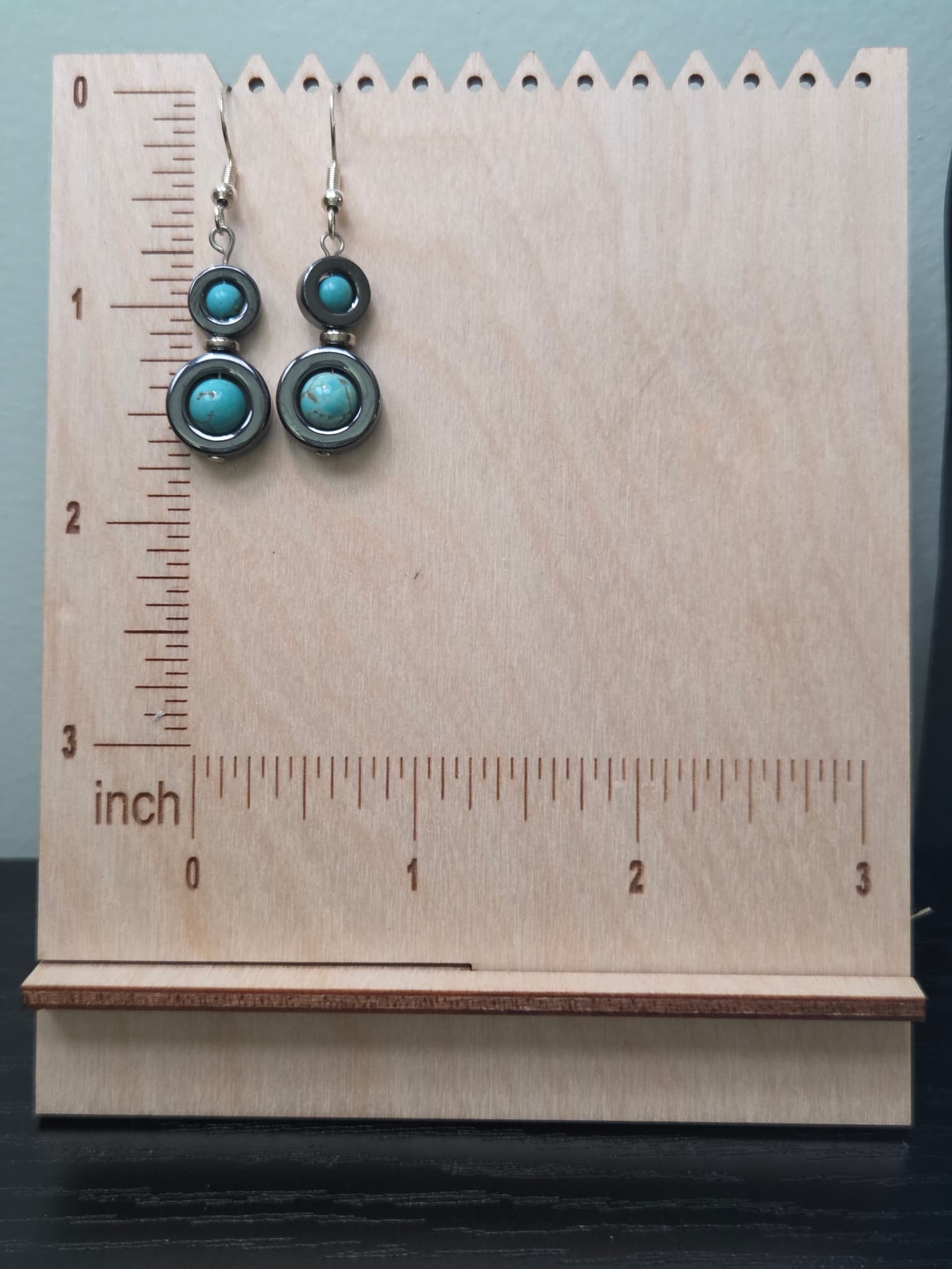 Hematite and turquoise howlite halo drop earrings displayed on a wooden earring stand with ruler for scale, showing approximately 1.5 inch length with silver fish hook ear wires