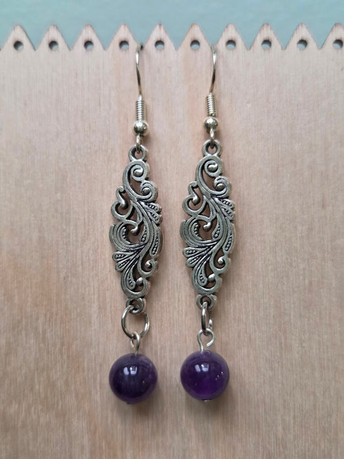 Amethyst gemstone drop earrings with ornate Tibetan silver filigree connector on wooden display stand with ruler for scale