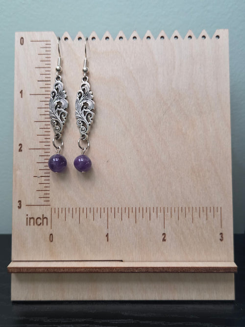 Close-up of handmade amethyst bead drop earrings featuring intricate antique silver filigree charm on kraft card background