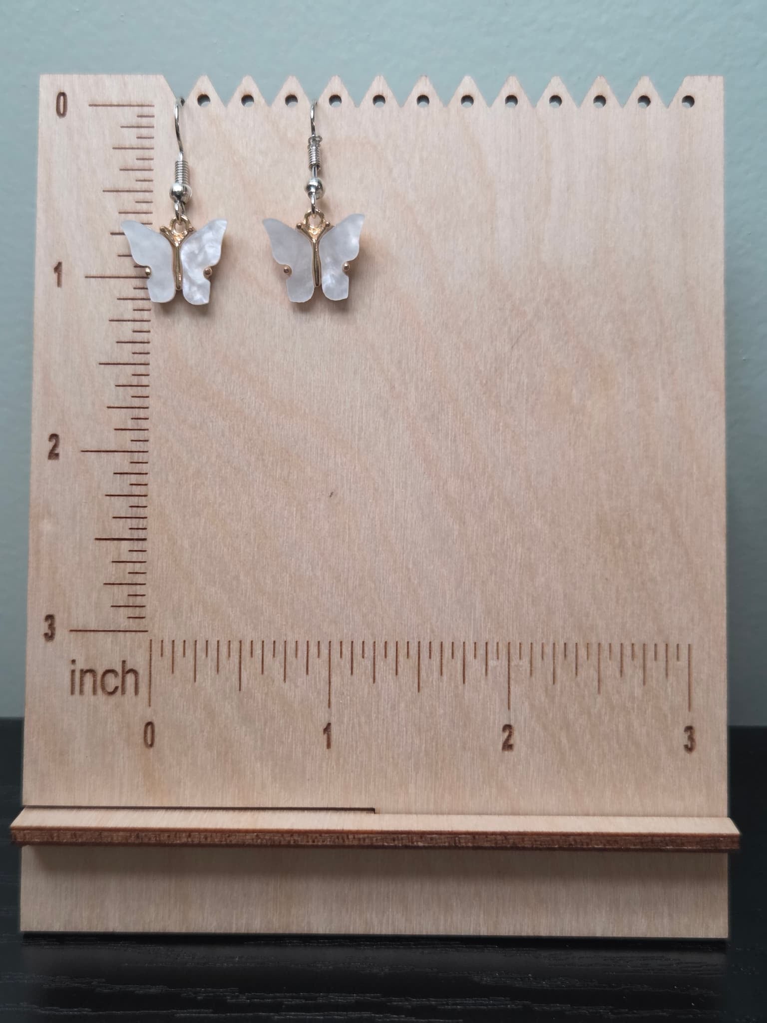 Mother-of-pearl shell butterfly dangle earrings displayed on a wooden earring stand with ruler for scale, showing approximately 1.5 inch length