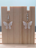 Close-up of mother-of-pearl shell butterfly earrings with gold-tone bail and silver fish hook ear wires, showing natural iridescent shimmer on white wings