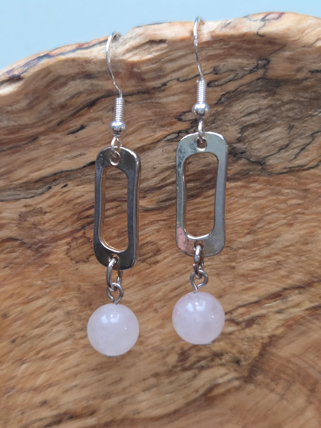 Close-up of rose quartz round bead earrings with reclaimed silver-tone link, shown on a wood grain surface