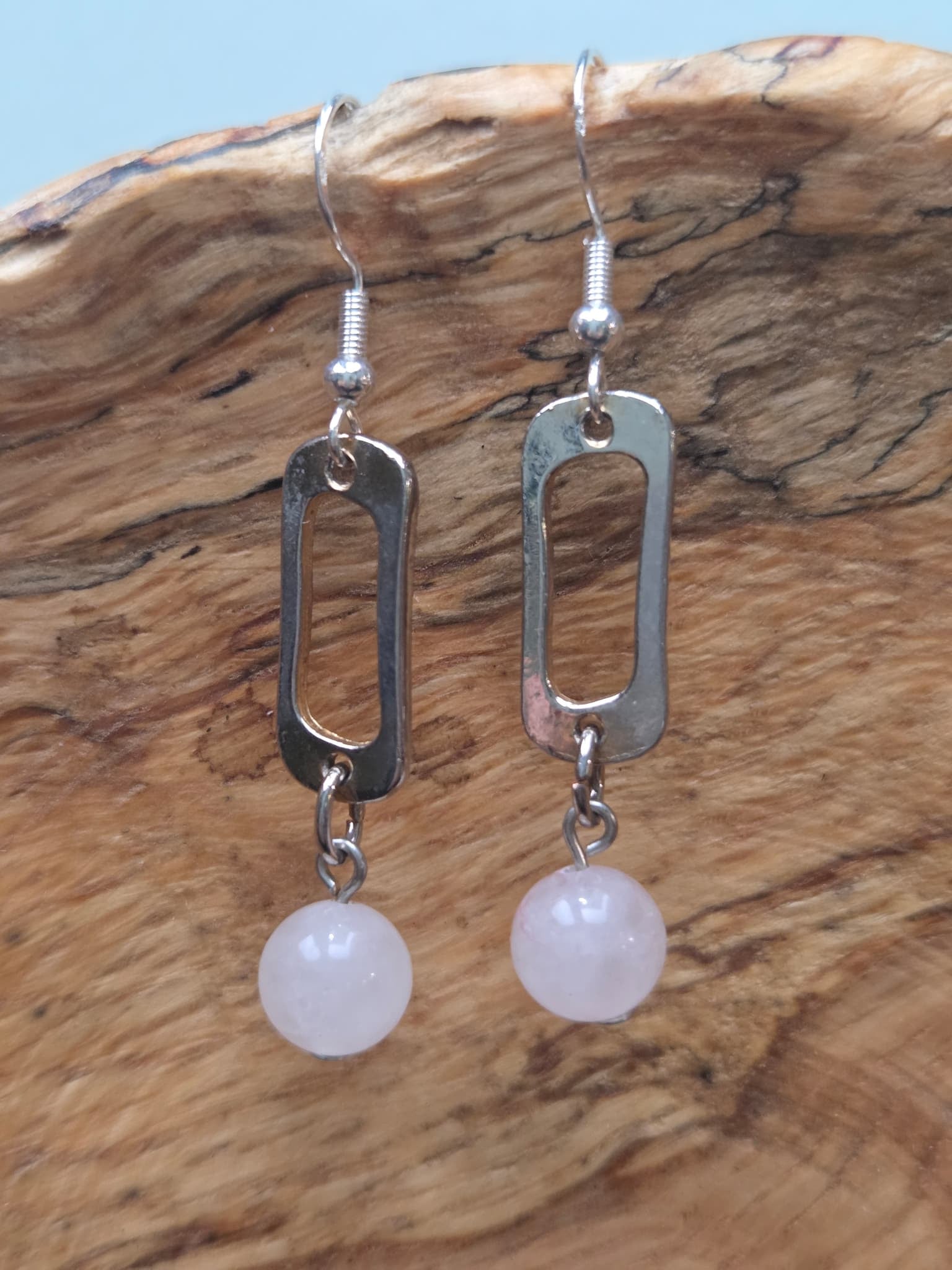 Close-up of rose quartz round bead earrings with reclaimed silver-tone link, shown on a wood grain surface
