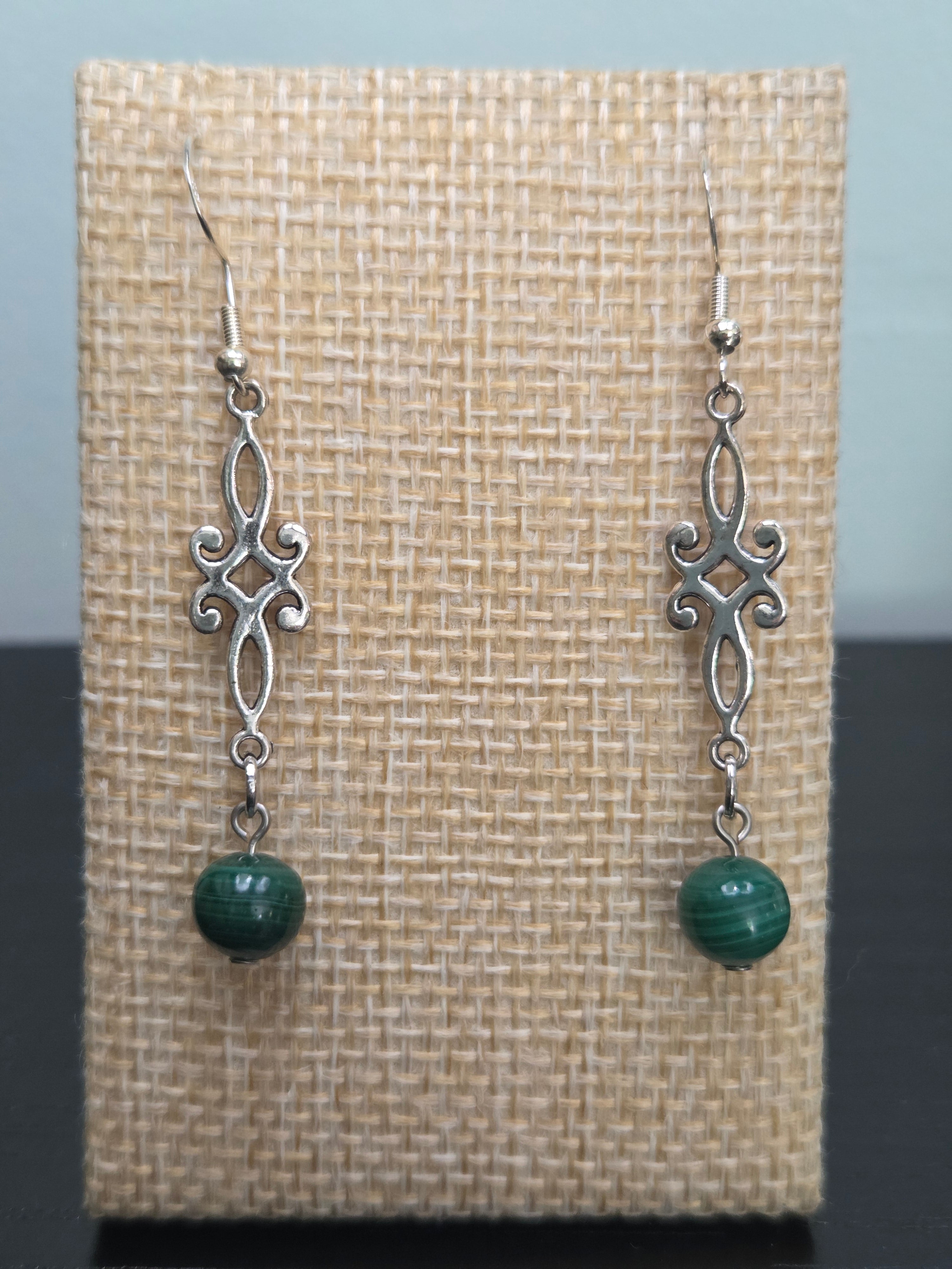 Close-up of silver-tone scrollwork drop earrings with genuine malachite beads