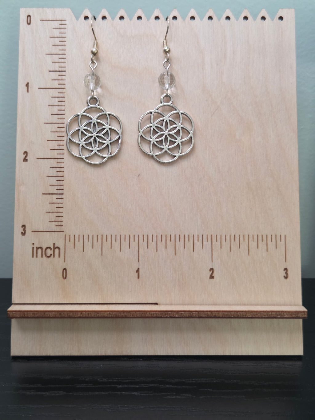 Seed of Life quartz dangle earrings displayed on a wooden earring stand with ruler showing approximately 2 inch length