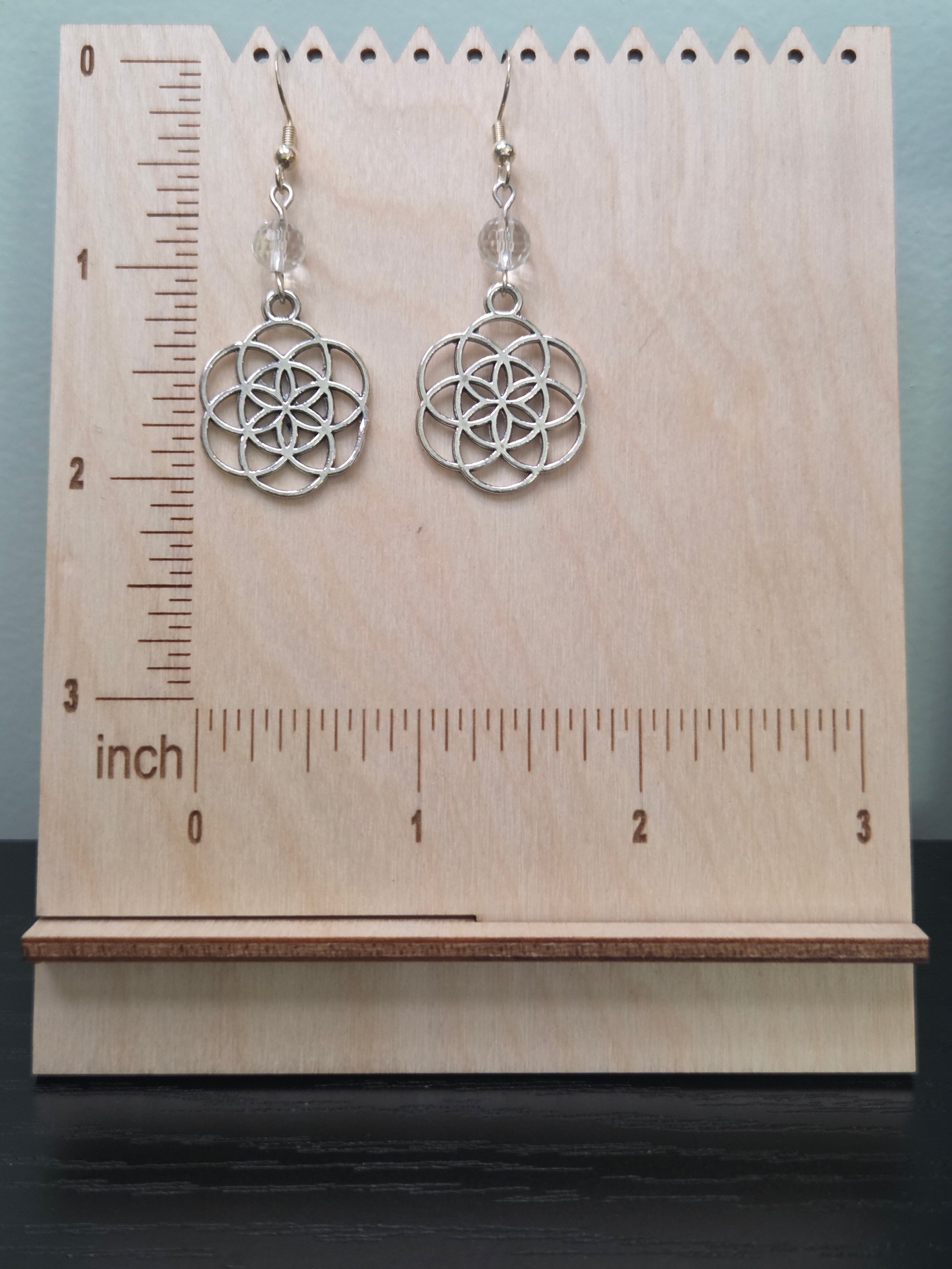 Seed of Life quartz dangle earrings displayed on a wooden earring stand with ruler showing approximately 2 inch length