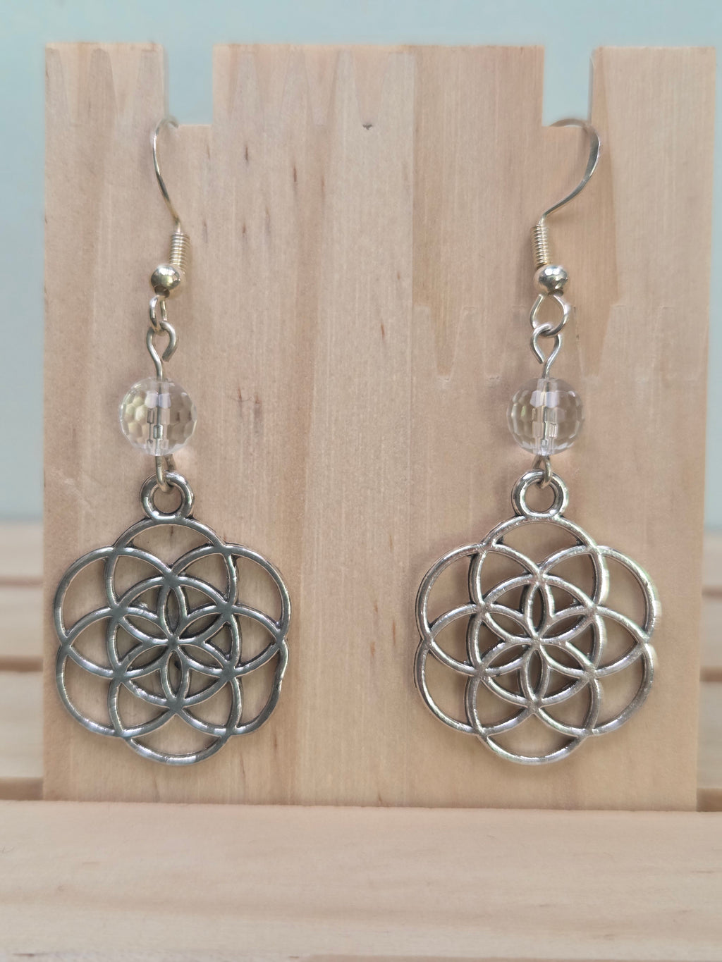Close-up of silver-tone Seed of Life charm earrings with faceted clear quartz beads