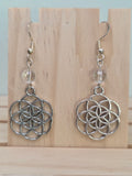 Close-up of silver-tone Seed of Life charm earrings with faceted clear quartz beads