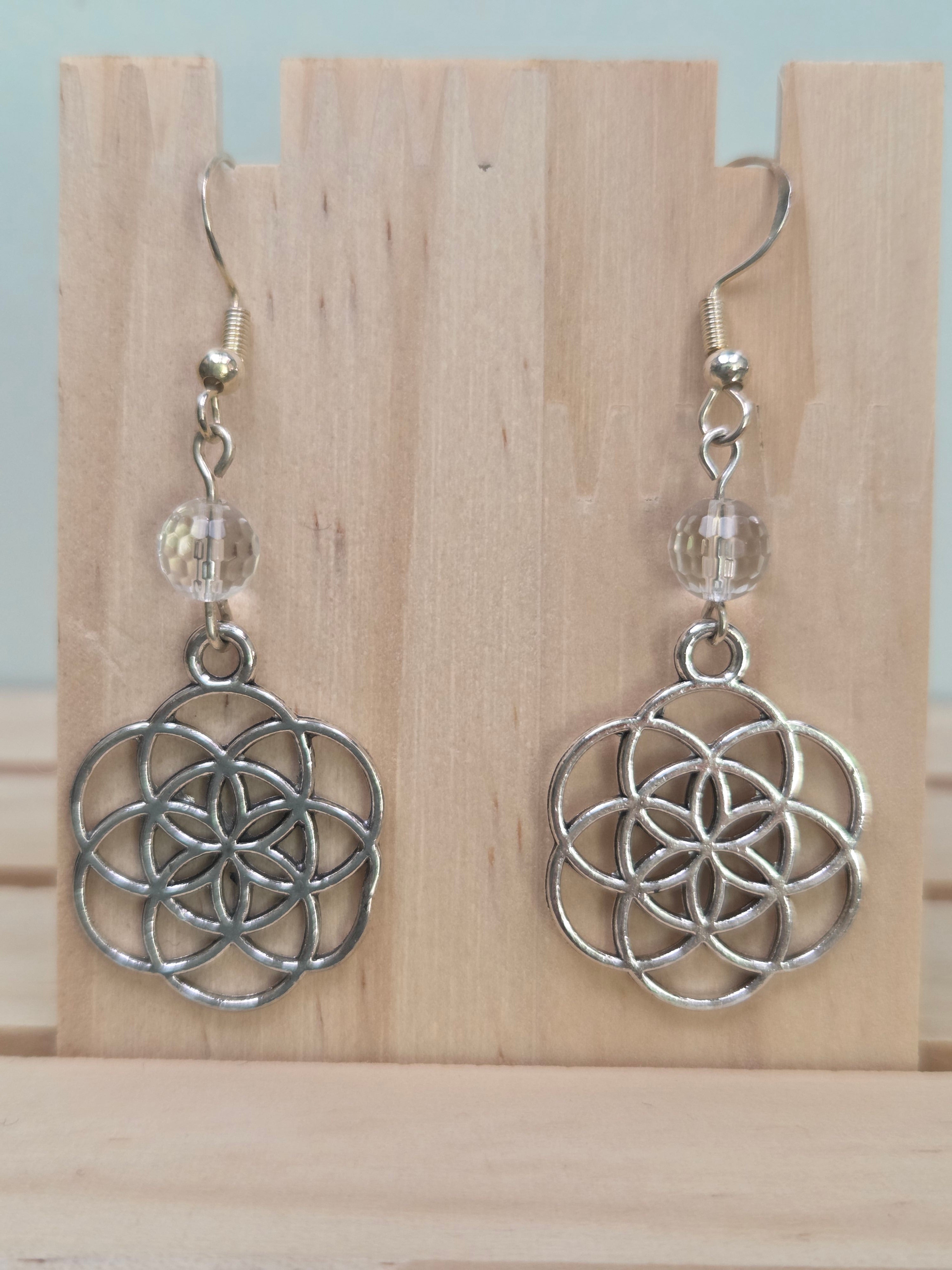 Close-up of silver-tone Seed of Life charm earrings with faceted clear quartz beads