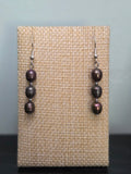 Peacock pearl stack drop earrings on woven fabric display, showing iridescent purple and bronze sheen