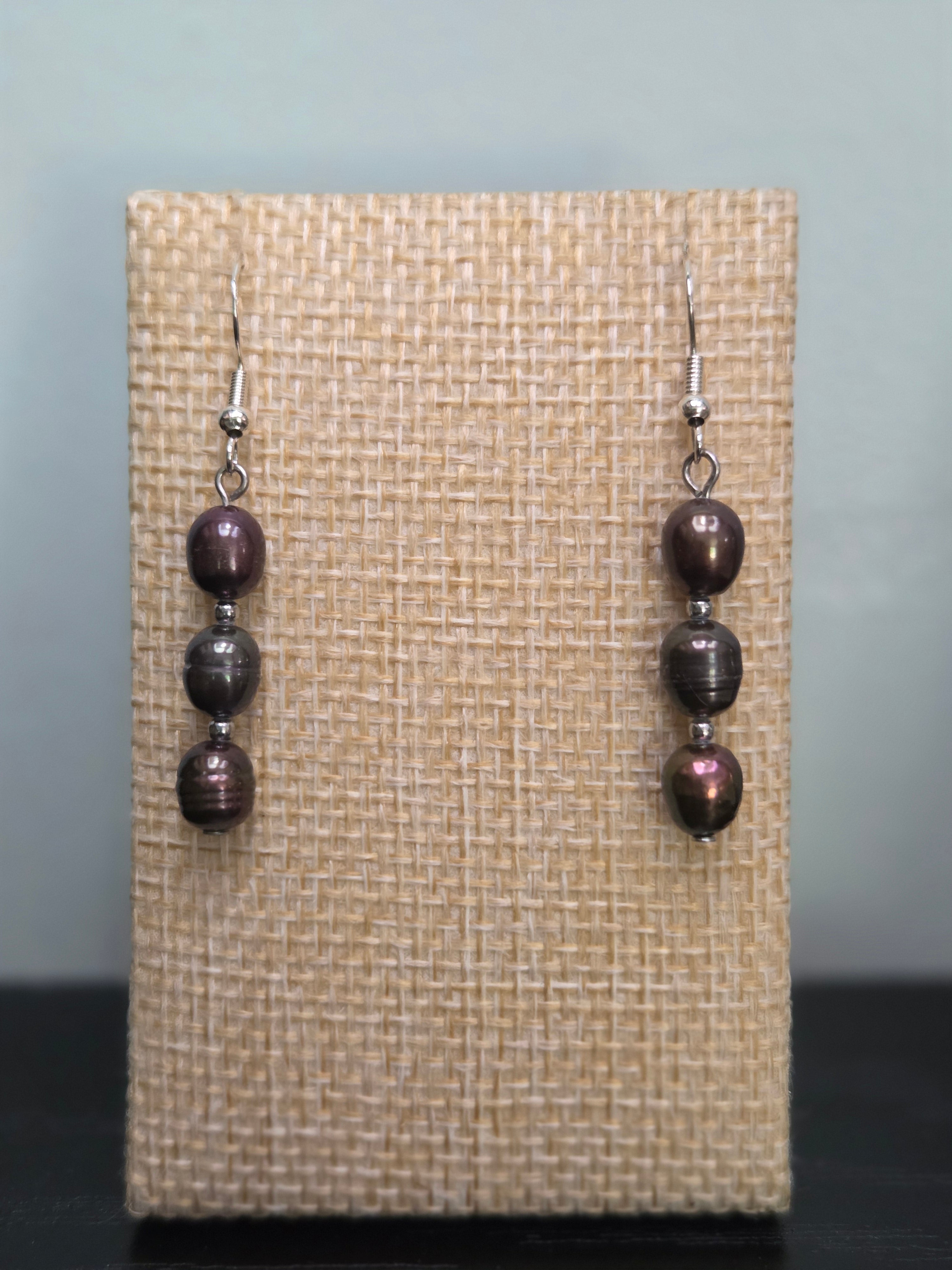 Peacock pearl stack drop earrings on woven fabric display, showing iridescent purple and bronze sheen
