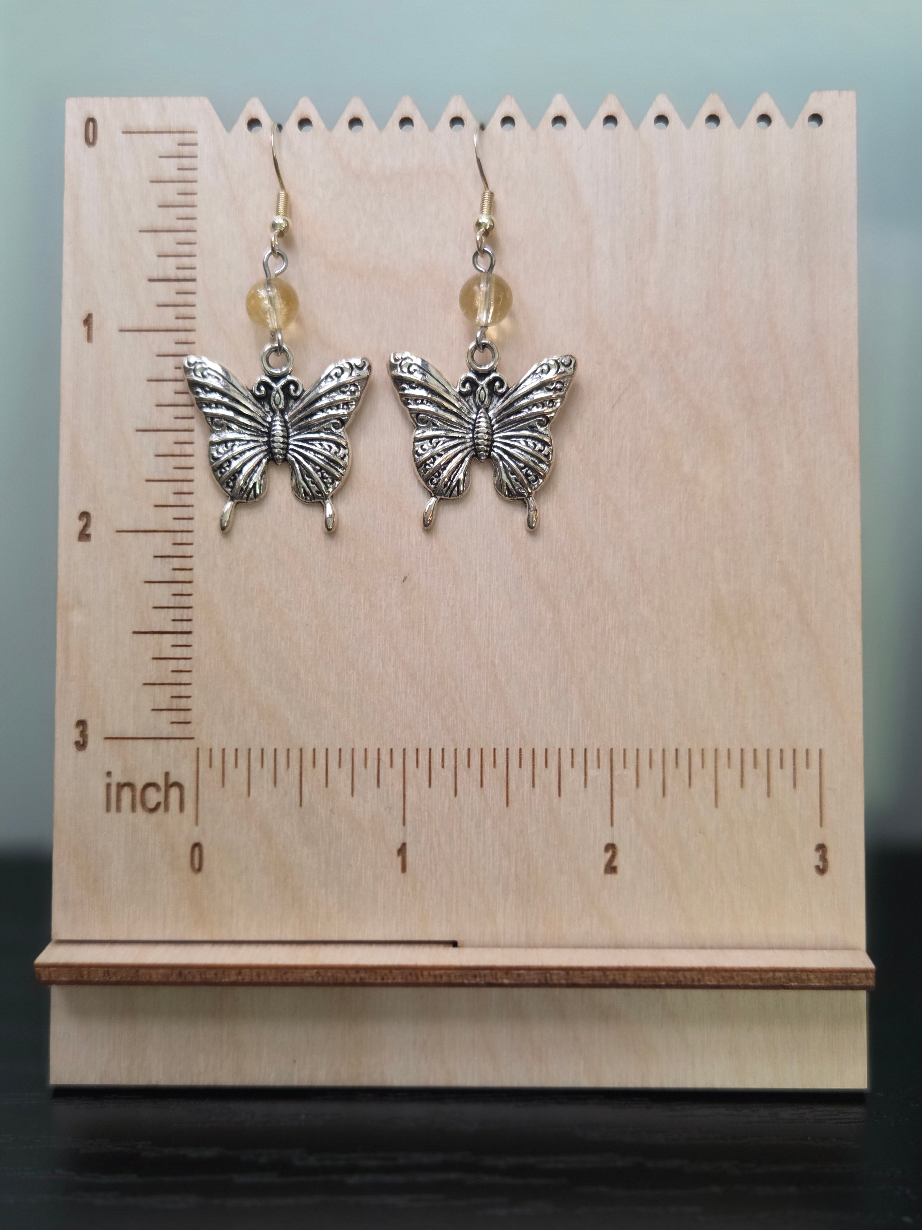 Butterfly citrine dangle earrings displayed on a wooden earring stand with ruler showing approximately 2 inch length