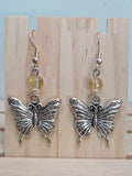Close-up of silver-tone filigree butterfly charm earrings with faceted citrine beads
