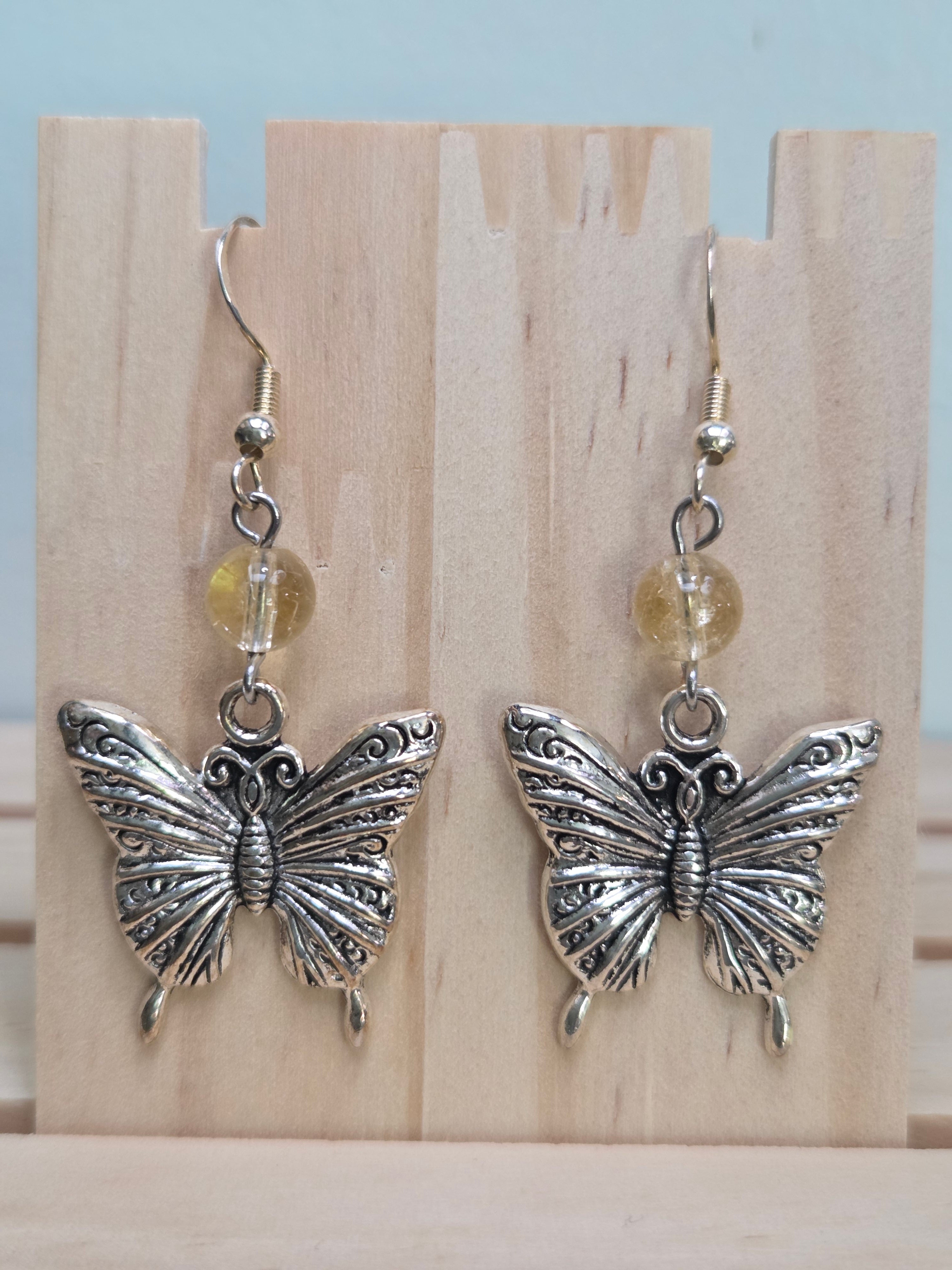 Close-up of silver-tone filigree butterfly charm earrings with faceted citrine beads