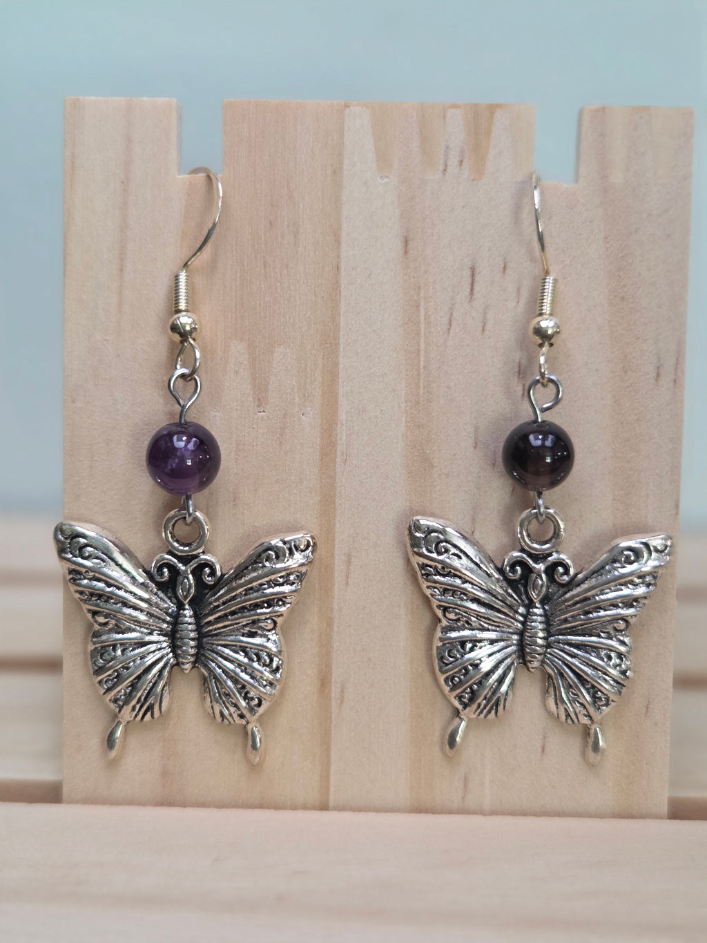 Close-up of silver-tone filigree butterfly charm earrings with amethyst round bead