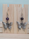 Close-up of silver-tone filigree butterfly charm earrings with amethyst round bead