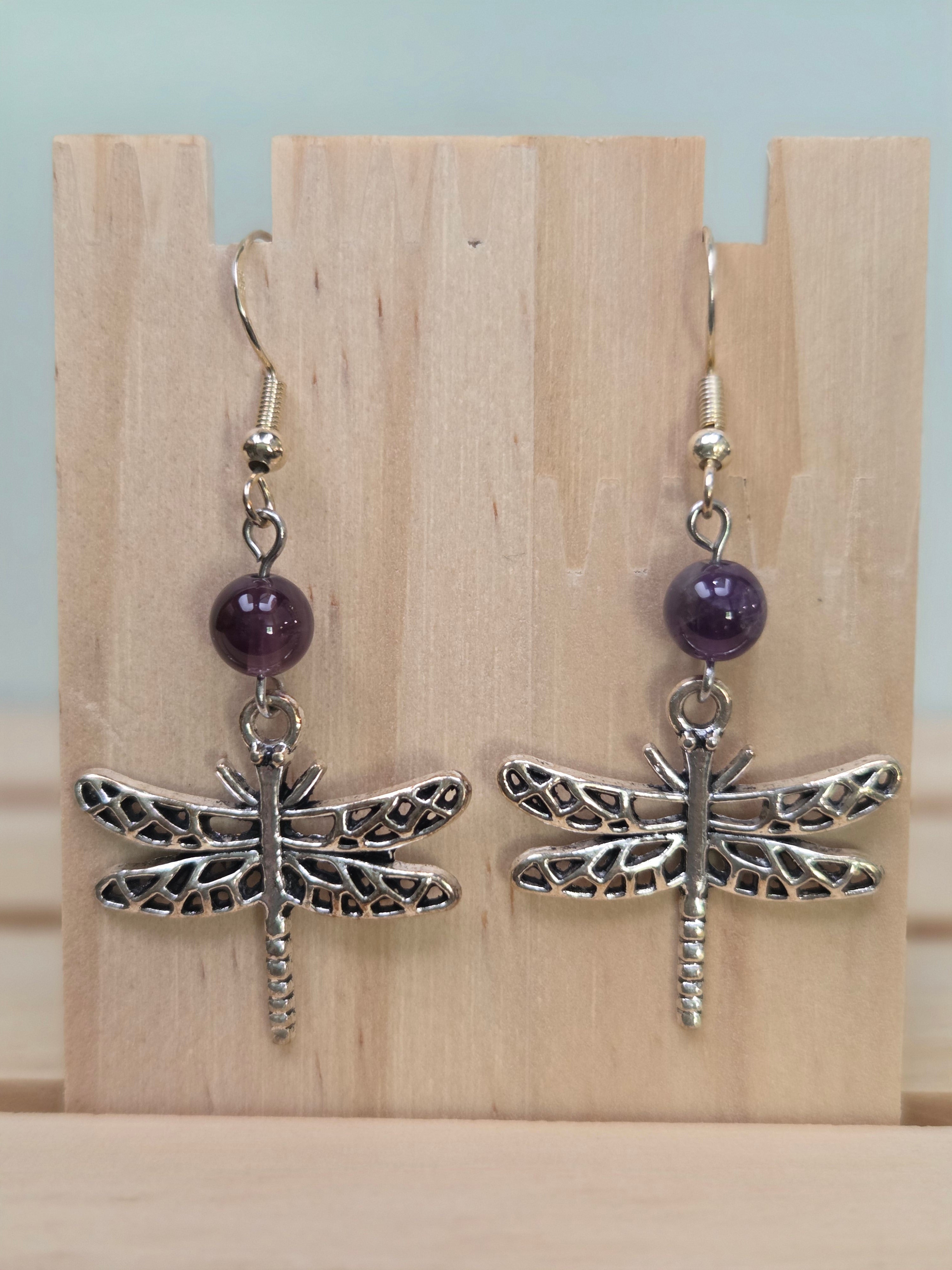 Close-up of silver-tone lattice dragonfly charm earrings with amethyst round bead