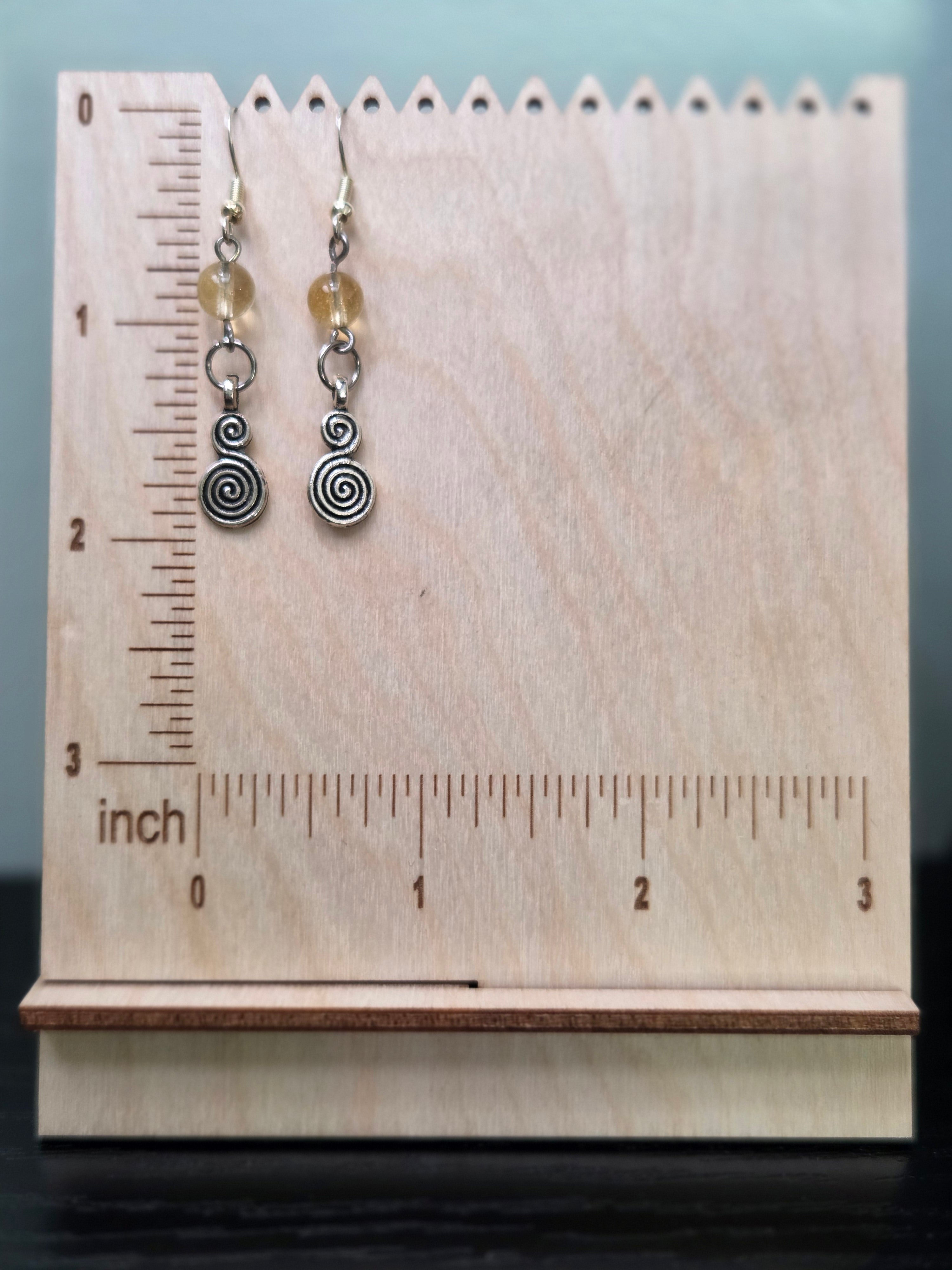 Spiral citrine dangle earrings displayed on a wooden earring stand with ruler showing approximately 2 inch length