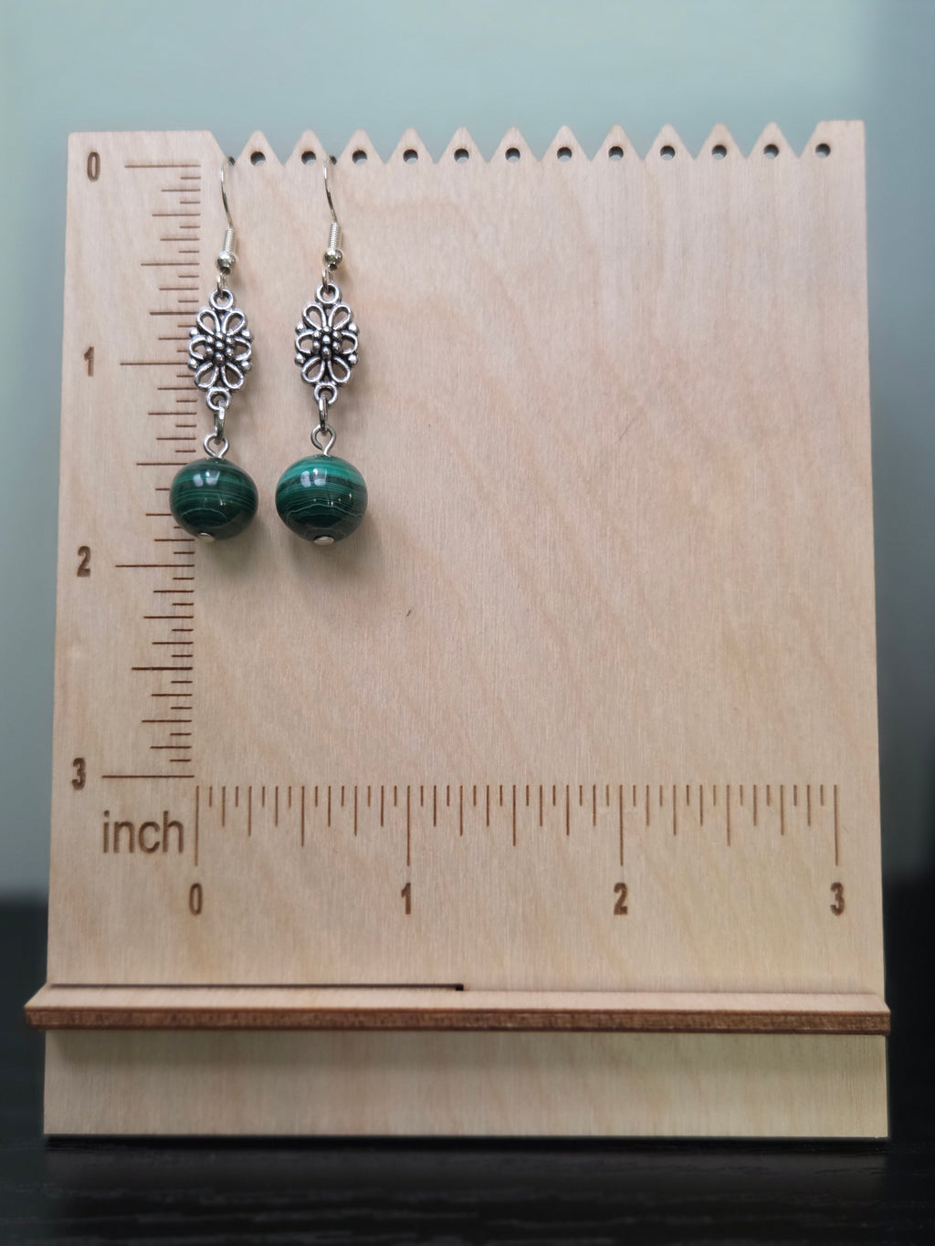 Malachite flower drop earrings displayed on a wooden earring stand with ruler showing approximately 1 7/8 inch length
