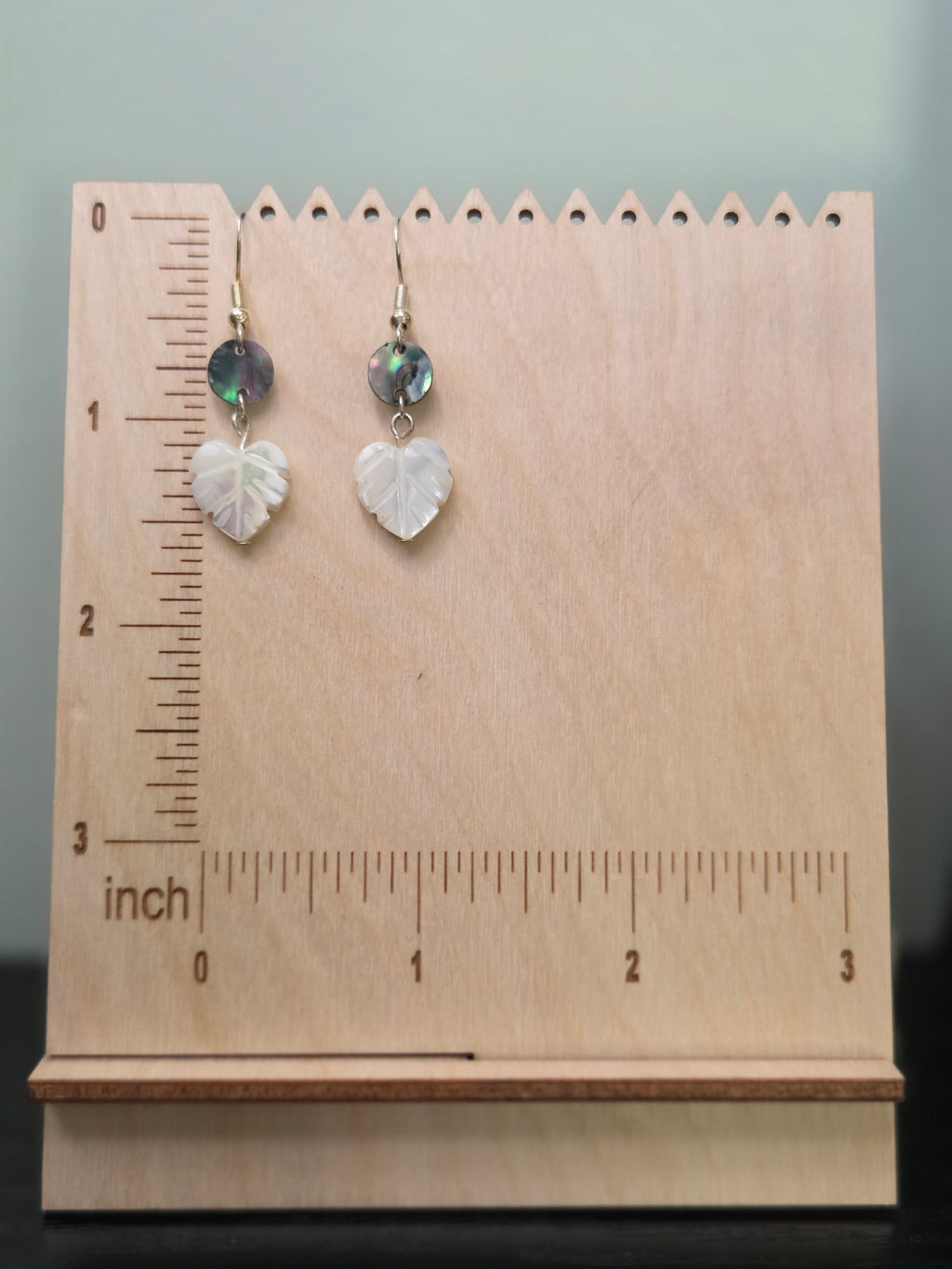 Abalone and mother-of-pearl leaf earrings displayed on a wooden earring stand with ruler showing approximately 1 7/8 inch length