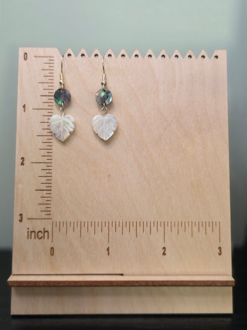 Abalone and mother-of-pearl leaf earrings displayed on a wooden earring stand with ruler showing approximately 1 7/8 inch length
