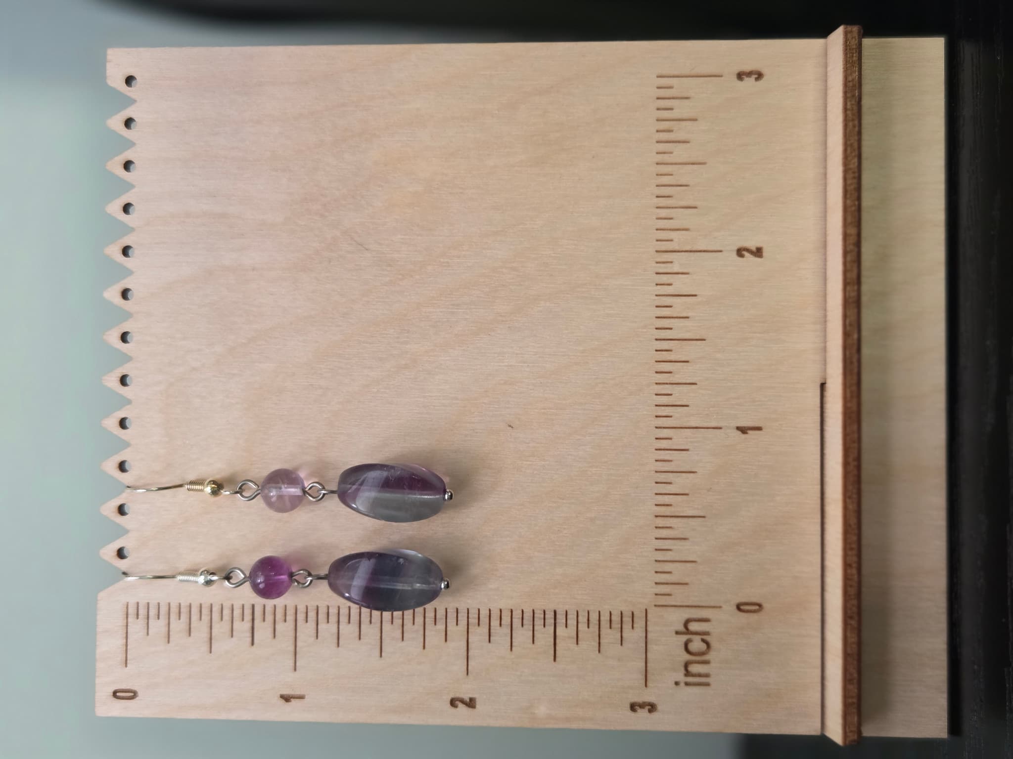 Fluorite drop earrings displayed on a wooden earring stand with ruler showing approximately 1.75 inch length
