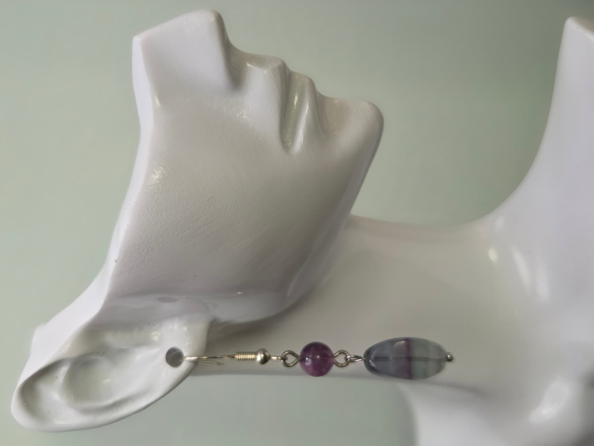 Fluorite drop earring worn on a white mannequin ear, showing banded purple and grey coloring