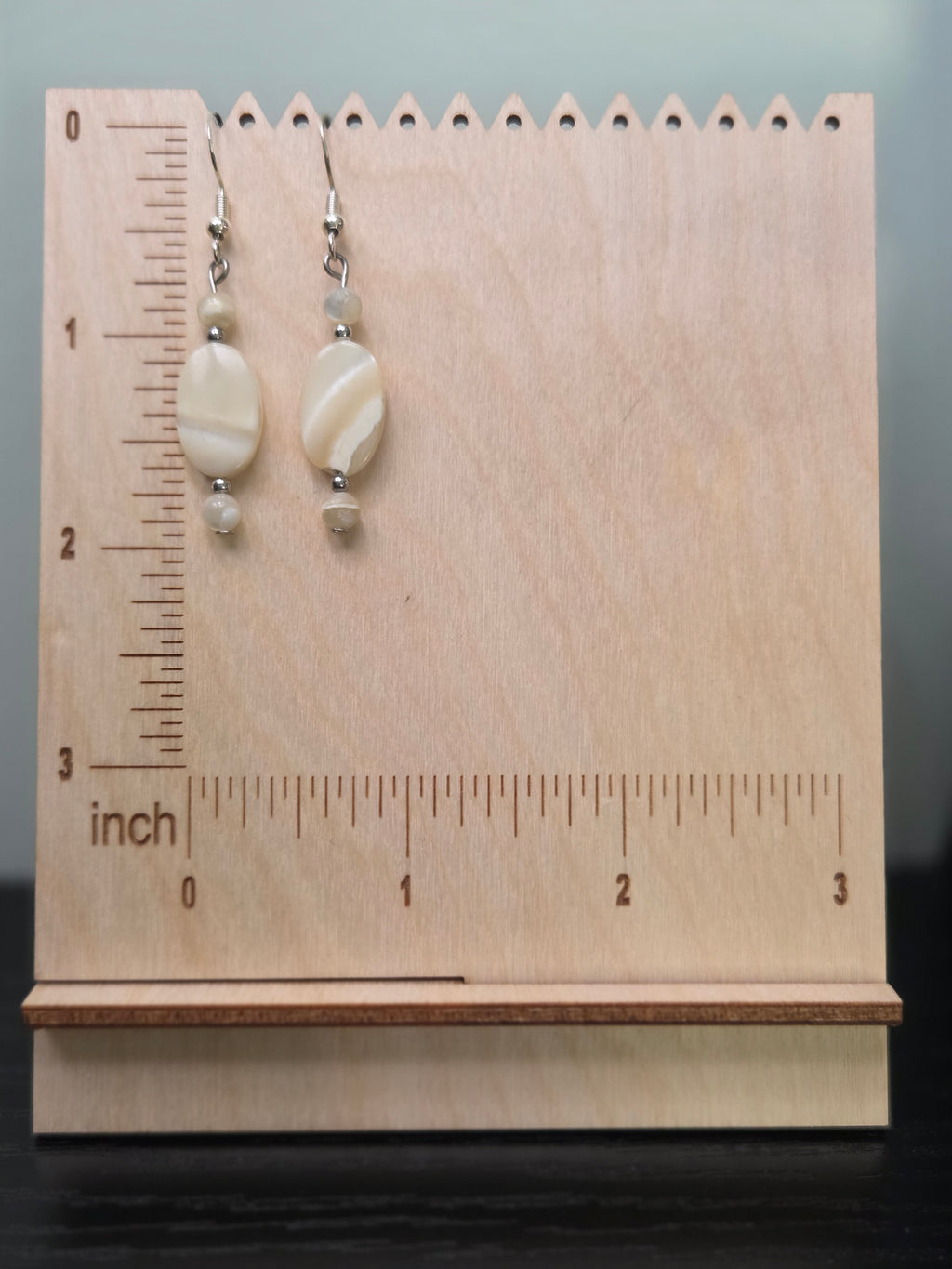 Shell dangle earrings displayed on a wooden earring stand with ruler showing approximately 1.75 inch length
