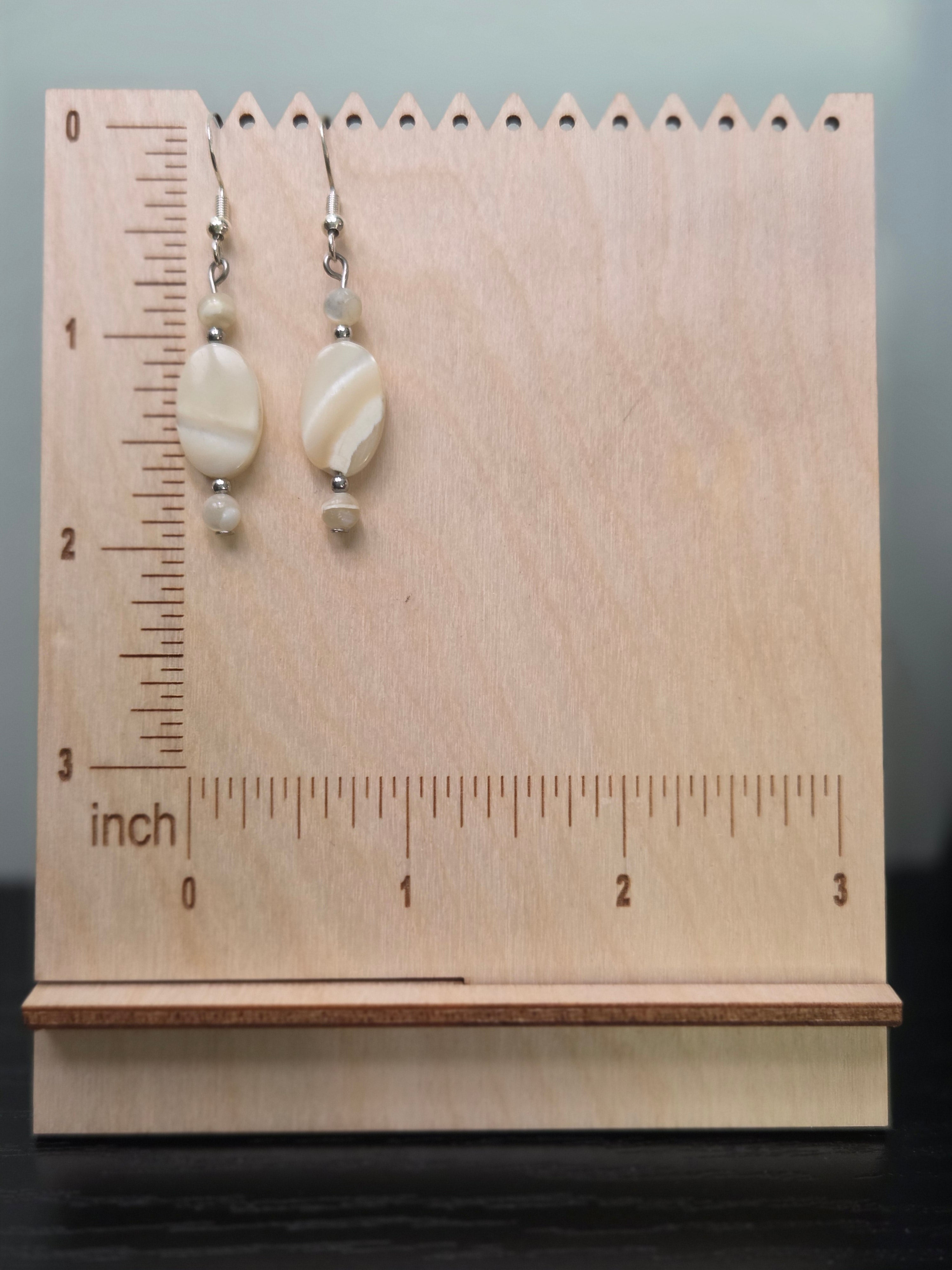 Shell dangle earrings displayed on a wooden earring stand with ruler showing approximately 1.75 inch length