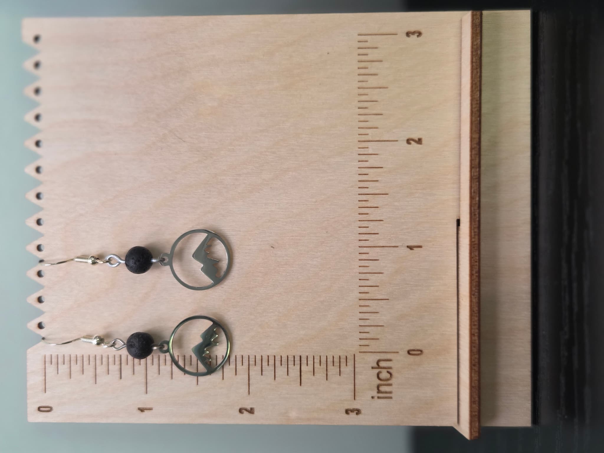 Mountain and lava stone drop earrings displayed on a wooden earring stand with ruler showing approximately 1.75 inch length