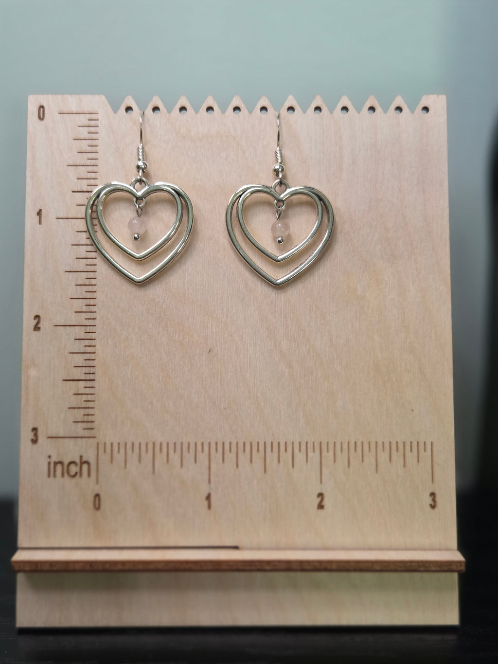 Silver-tone double heart rose quartz earrings on wooden ruler board showing approximately 1.4 inch length