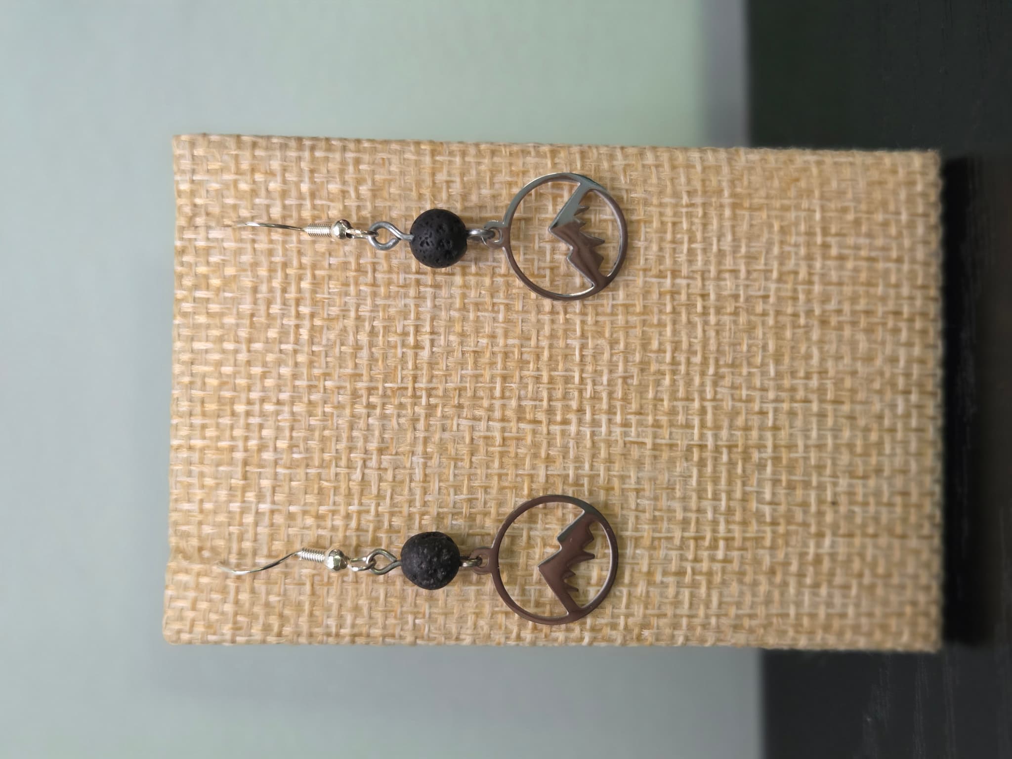 Close-up of lava stone bead and stainless steel mountain charm earrings