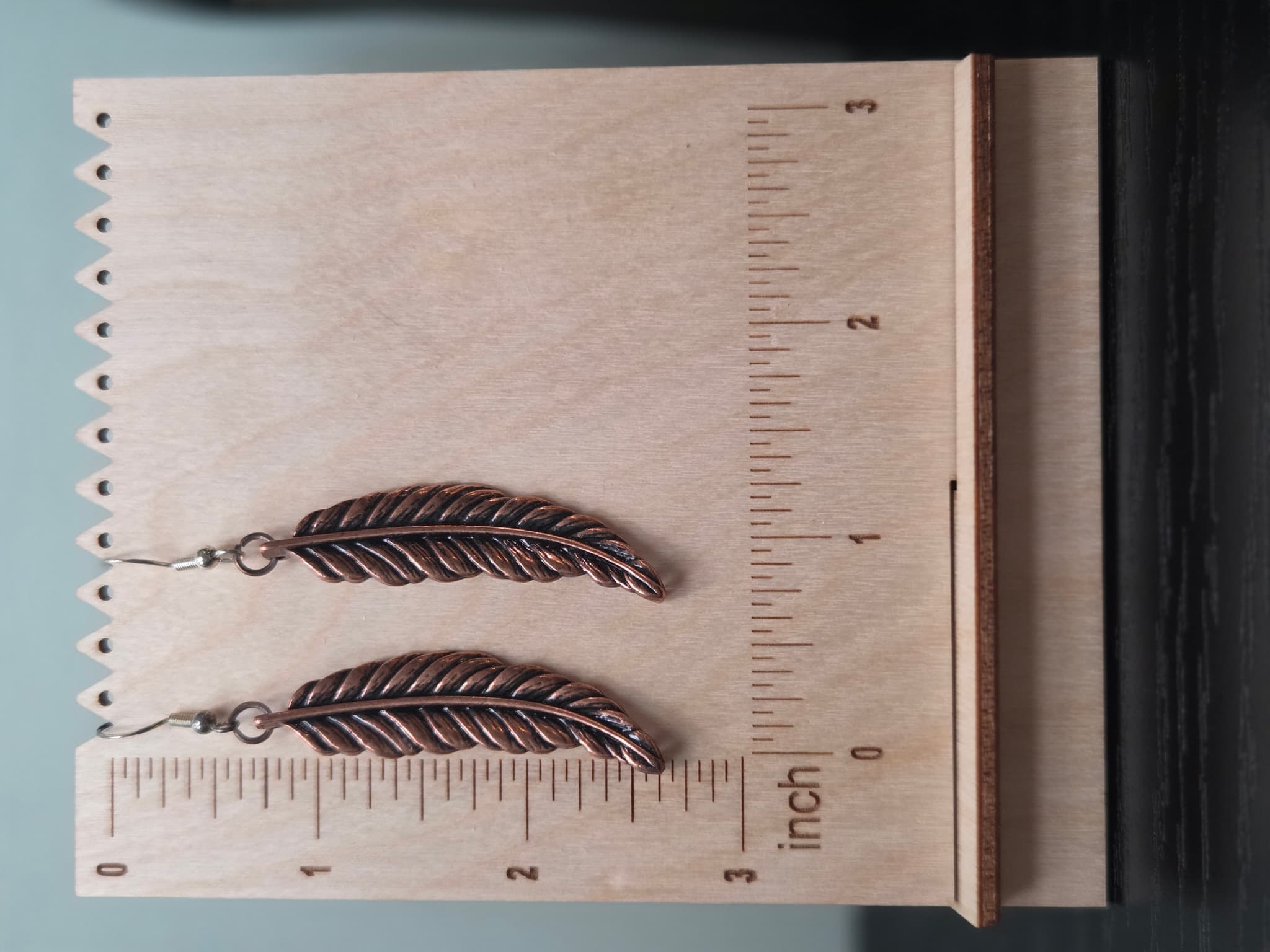 Pair of reclaimed copper-tone feather drop earrings shown against a woven burlap display card