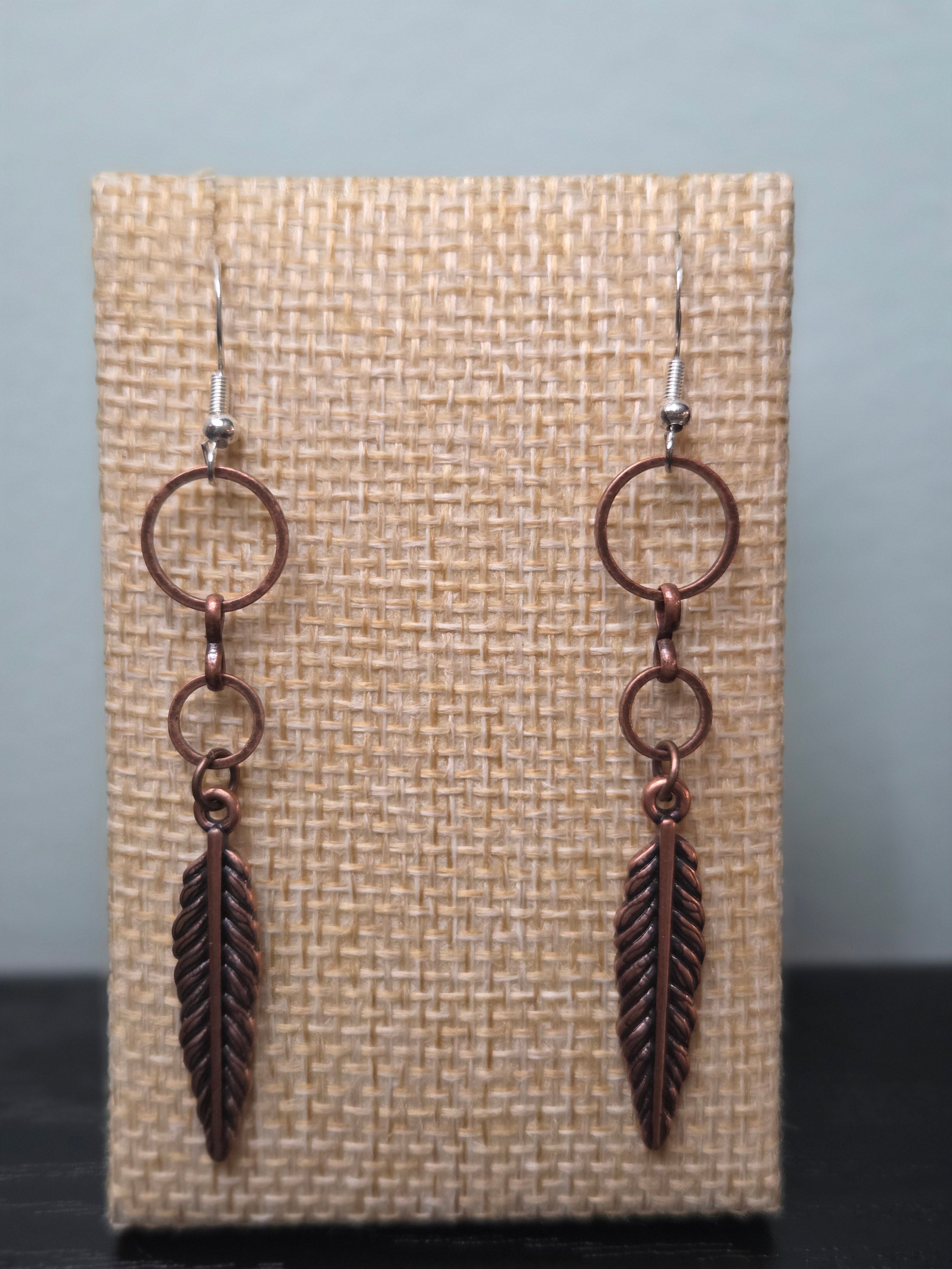 Pair of reclaimed copper-tone feather cascade earrings with double connector rings shown against a woven burlap display card